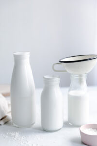 three bottles with coconut milk with white background and one white milk funnel in a bottle