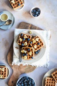 waffles on a plate on a white napkin on a wooden cutting board with a small bowl with syrup