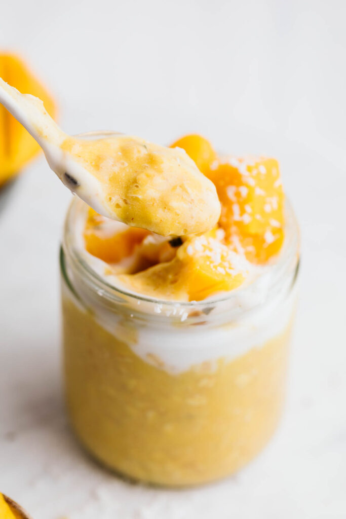 Mango Overnight Oats in a glass pot with a spoon taking out a scoop.