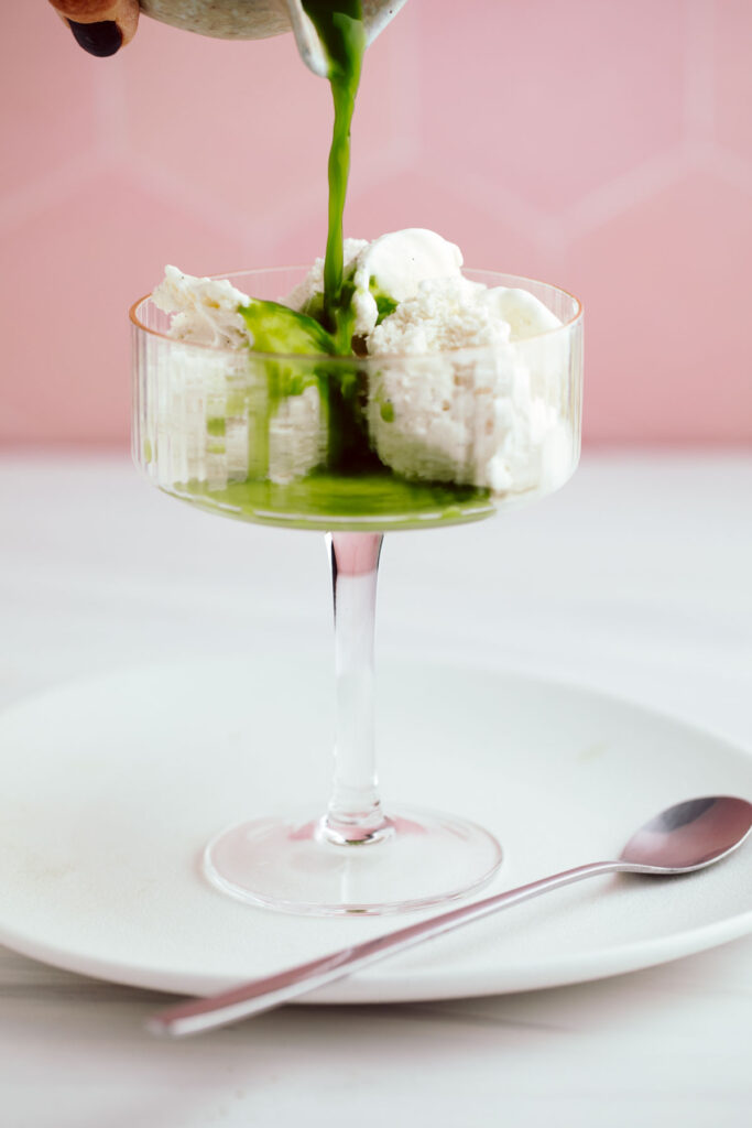 Pouring freshly whisked matcha over vanilla ice cream in a glass.