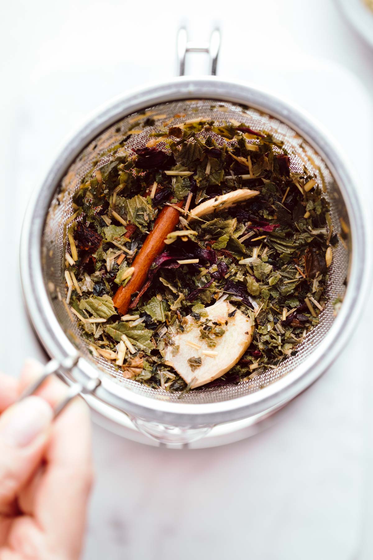 A large strainer with wet brewed herbs, a cinnamon stick and ginger pieces.