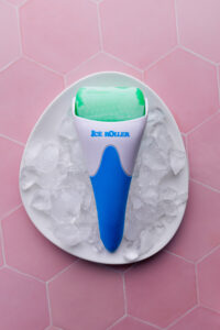 ice face roller on a white plate with ice cubes on a pink tile backdrop