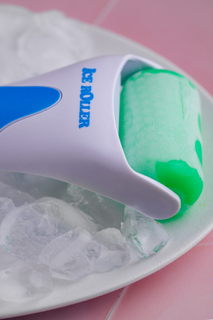 ice face roller with a frozen roller top on a white plate with ice cubes on a pink tile backdrop