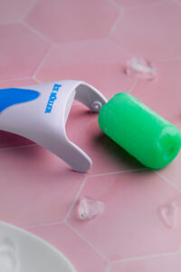 ice face roller with a melted roller detached from it on a pink tile backdrop with melted ice cubes