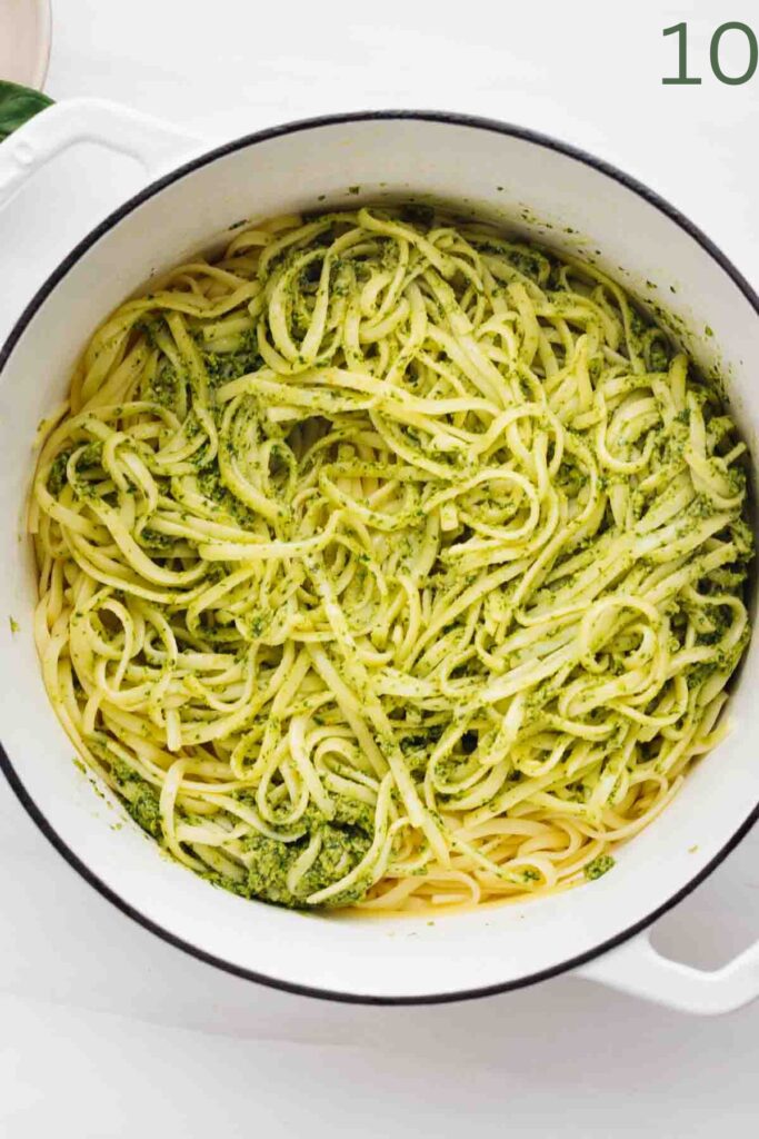 A big white pot with cooked linguine pasta mixed with basil pesto in it.