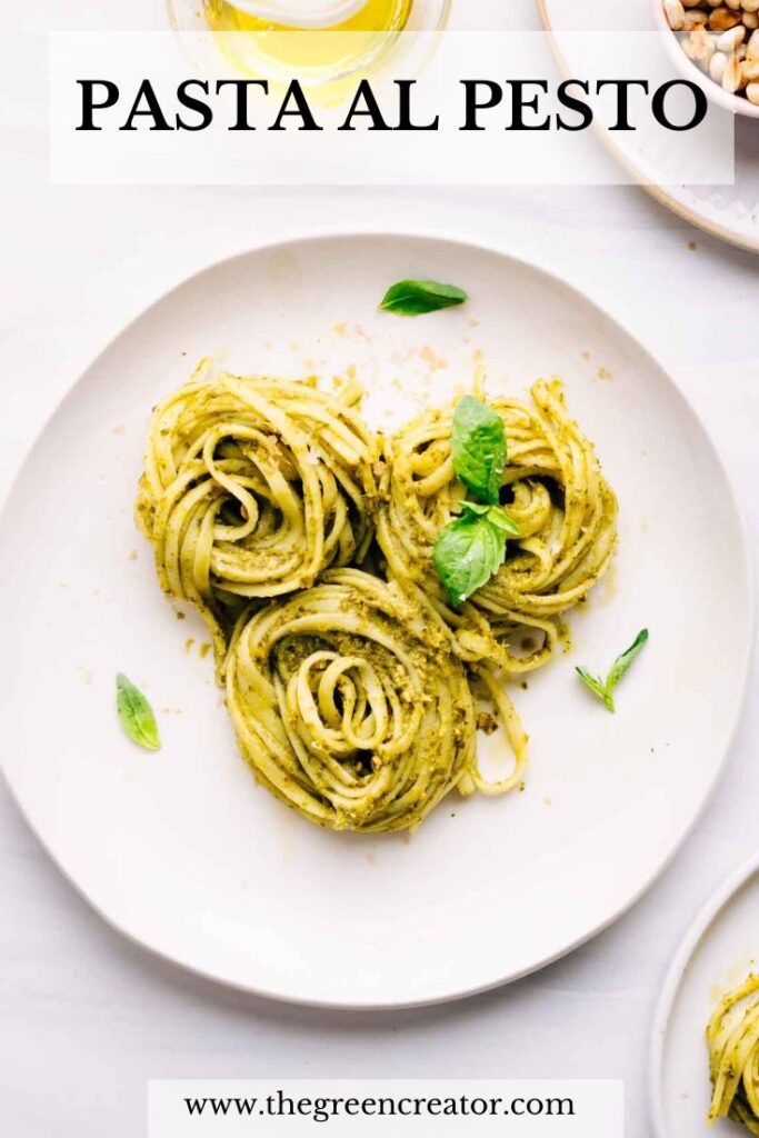 A light colored plate on a white backdrop with three swirls of pasta al pesto on it and basil leaves as a garnish with the text pasta al pesto written on top above the plate.