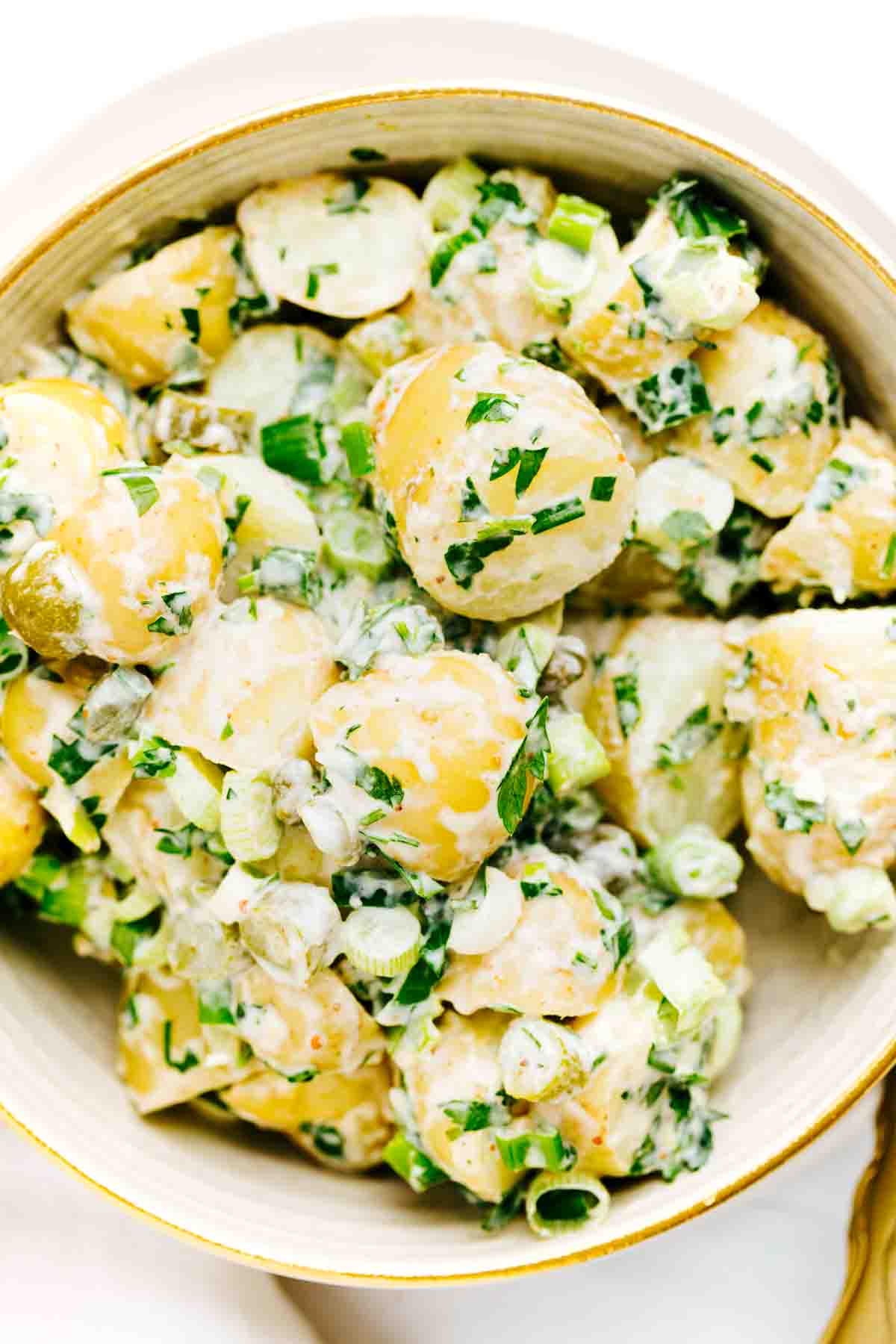 Potato salad with spring onions, herbs and a dressing in a round bowl.