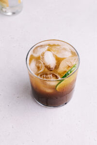 A glass with cold brew tonic with ice cubes and a slice of lime seen from slightly above on a light grey backdrop