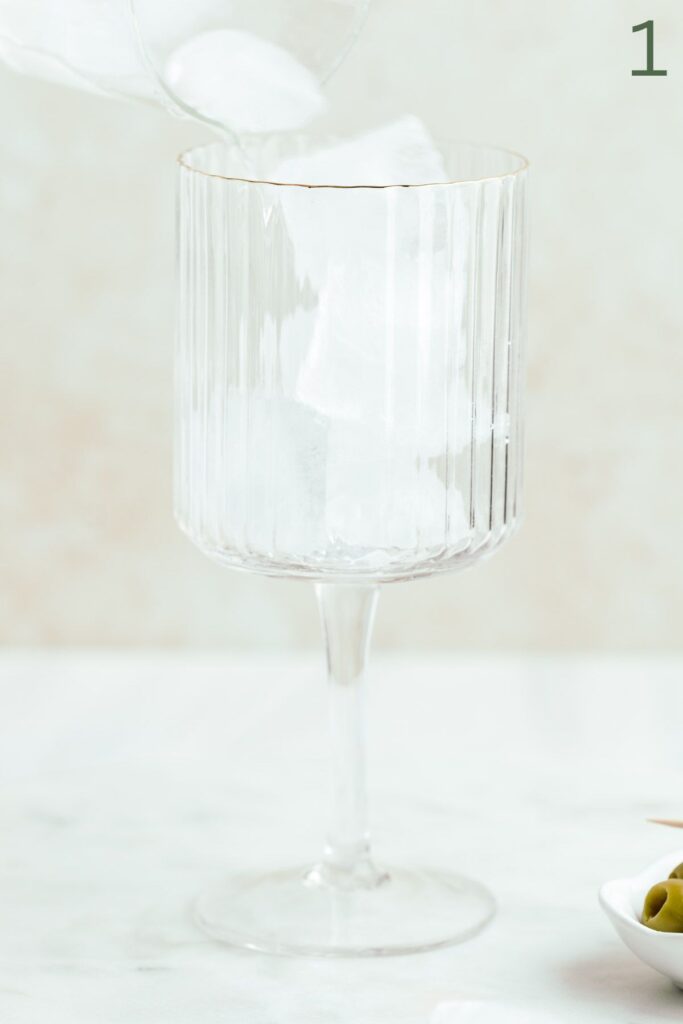Ice cubes being poured into a wine glass with a stem on a marble backdrop.