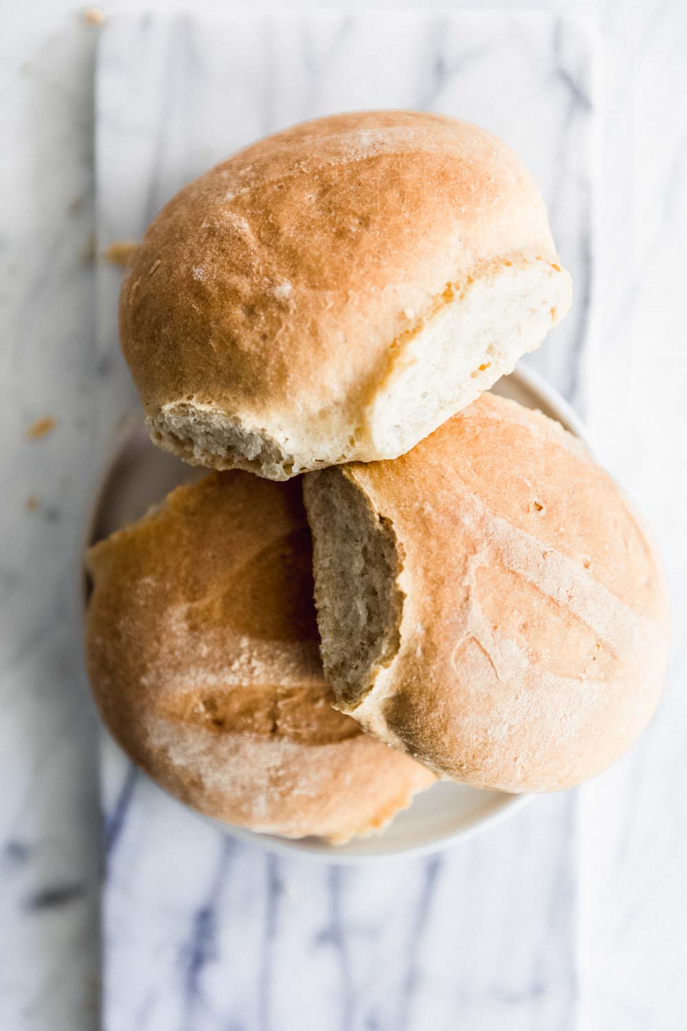 three dinner rolls stacked in a circle on a small white plate on a white marble backdrop