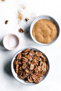 pecans, coconut sugar and salt in small bowls on a white backdrop