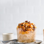 Pumpkin Pie Overnight Oats on a white backdrop in a small glass on a light blue plate with a small bowl in the background