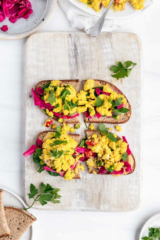 Open sandwich with scrambled tofu on it with spinach and red pickled cabbage on a white wooden cutting board