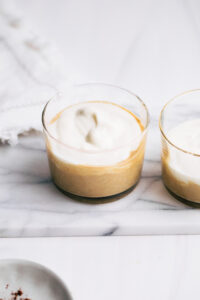 Two small jars with a layer of overnight tiramisu oats and a layer of yogurt on white marble