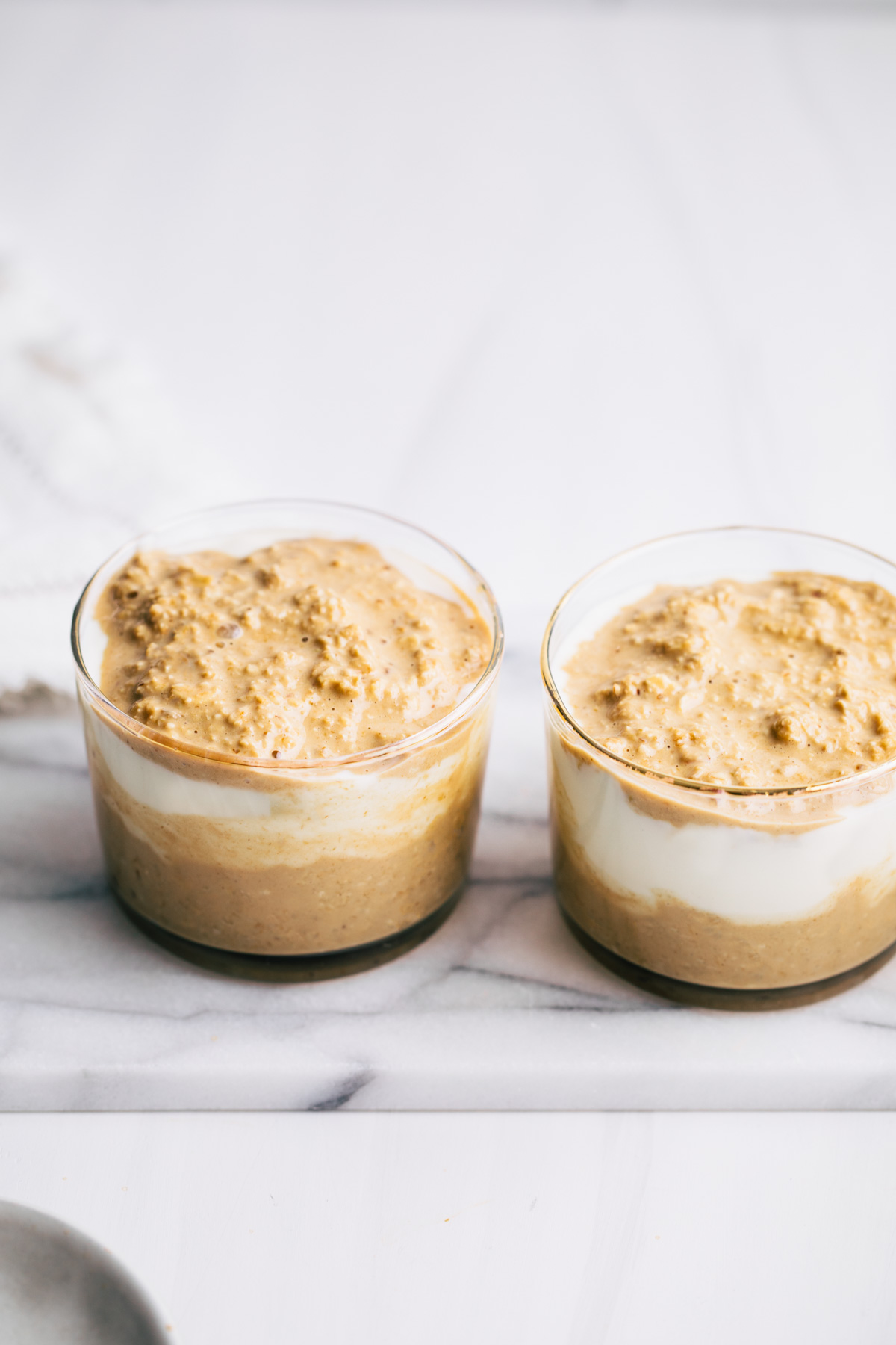 Two small jars with a layer of overnight tiramisu oats with a layer of yogurt and a layer of oats on white marble
