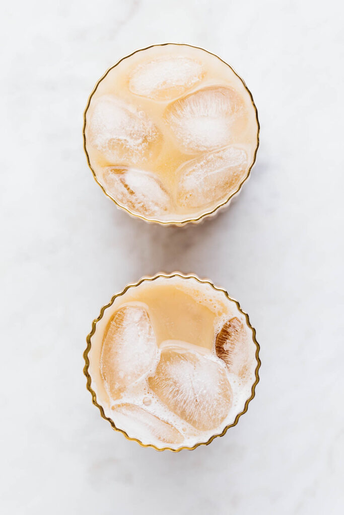 Top view of two ribbed glasses with a golden rim filled with a light brown drink with ice cubes.