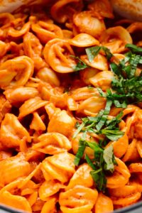 Closeup of orange colored shell pasta sprinkled with chopped basil on the right side.