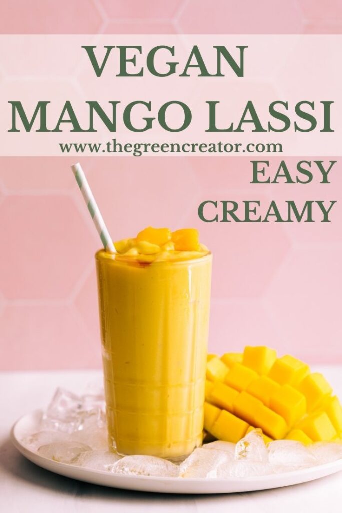 Mango lassi in a tall glass with a straw on a plate with ice cubes and fresh mango in front of a pink tile backdrop