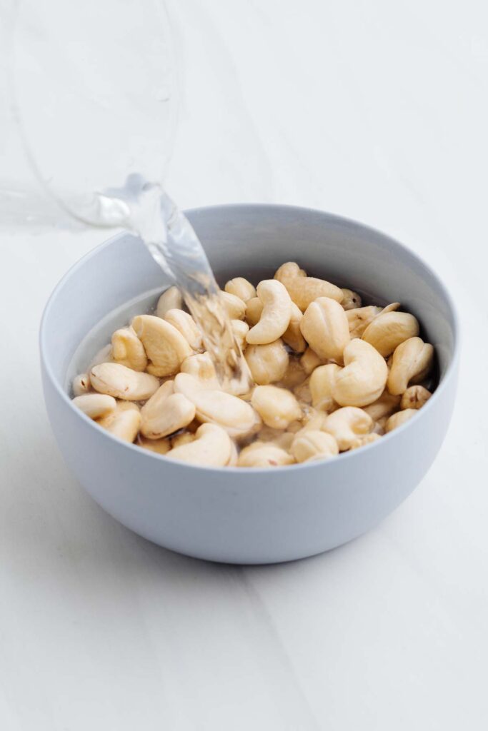 A small bowl with cashews with water being poured over it.