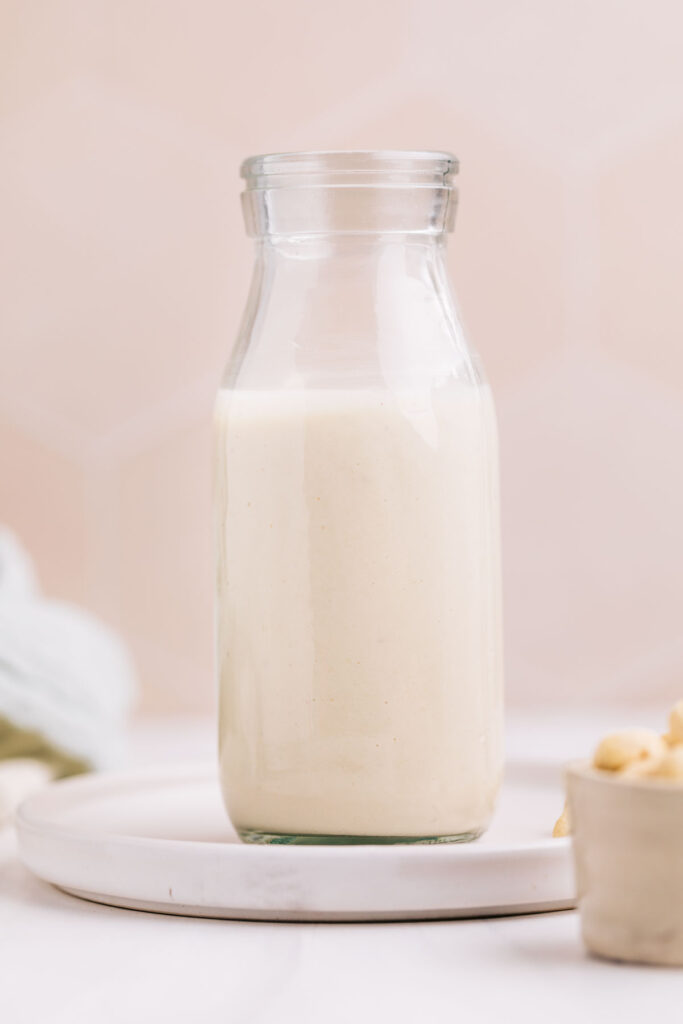 A glass jar on a plate with white bechamel sauce in it in front of a beige backdrop.