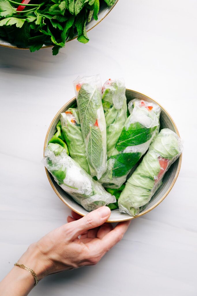 A hand holding a bowl with summer rolls in it on a white backdrop