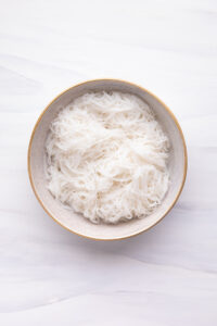 A bowl with cooked rice vermicelli on a white backdrop