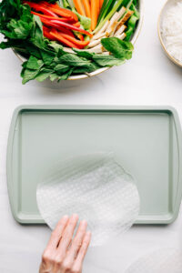 A light green baking tray filled with a bit of water and a hand dipping rice paper in it