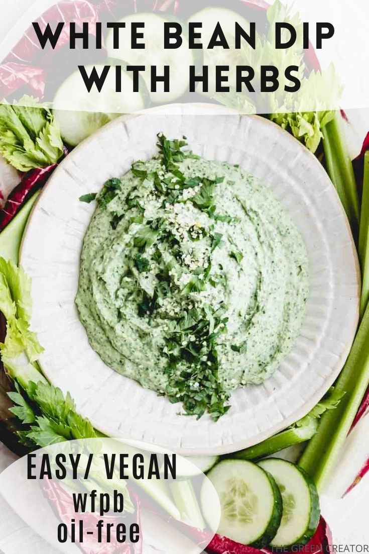 white bean dip in bowl with green herbs as topping on a backdrop of raw vegetables with text for pinterest