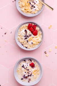 three blue bowls with porridge topped with berries and coconut on a pink tile backdrop