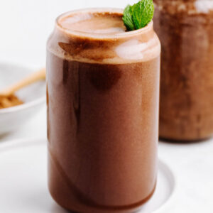 Brown carob smoothie on a white plate decorated with a mint leave.