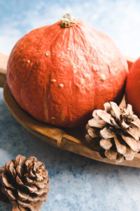 Two pumpkins in a wooden bowl on a blue backdrop next to two pine apples