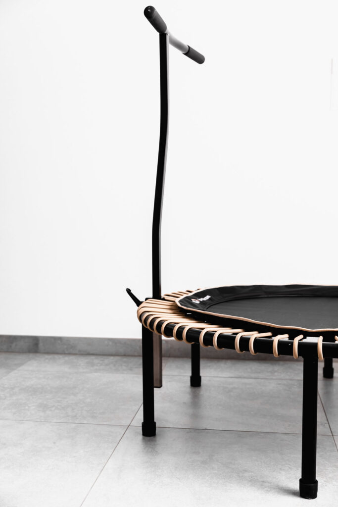 black bellicon rebounder with a stability bar on a grey floor with a white wall