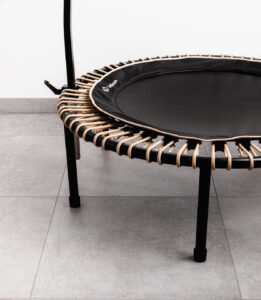 black bellicon rebounder with a stability bar on a grey floor with a white wall