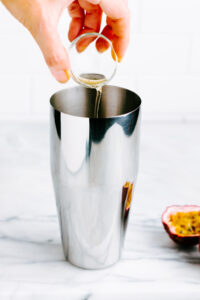 a silver colored cocktail shaker with apple cider vinegar being poured into it