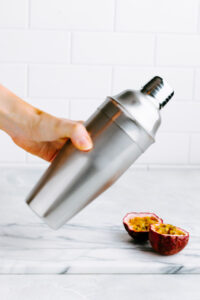 a cold silver colored cocktail shaker on a white backdrop with a hand shaking it