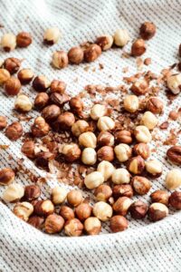 a light colored kitchen towel with hazelnuts on it with the skin removed of most of them.