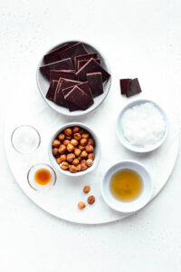 the ingredients for chocolate torrone on a round marble cutting board in small bowls.
